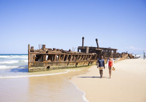 Couple walking along the beach past the historic shipwreck